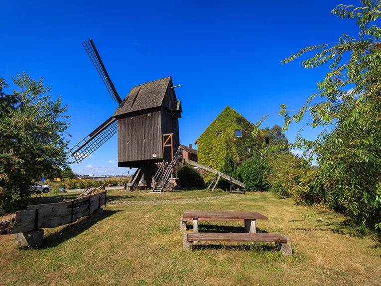 Eine alte Mühle aus Holz im Grünen mit Parkbänken in der Umgebung.