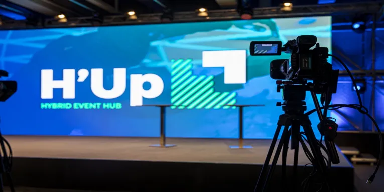 H'Up Hybrid Event Hubi lava, millel on suur LED-ekraan, kaks baarilauad ja kaamera esiplaanil.