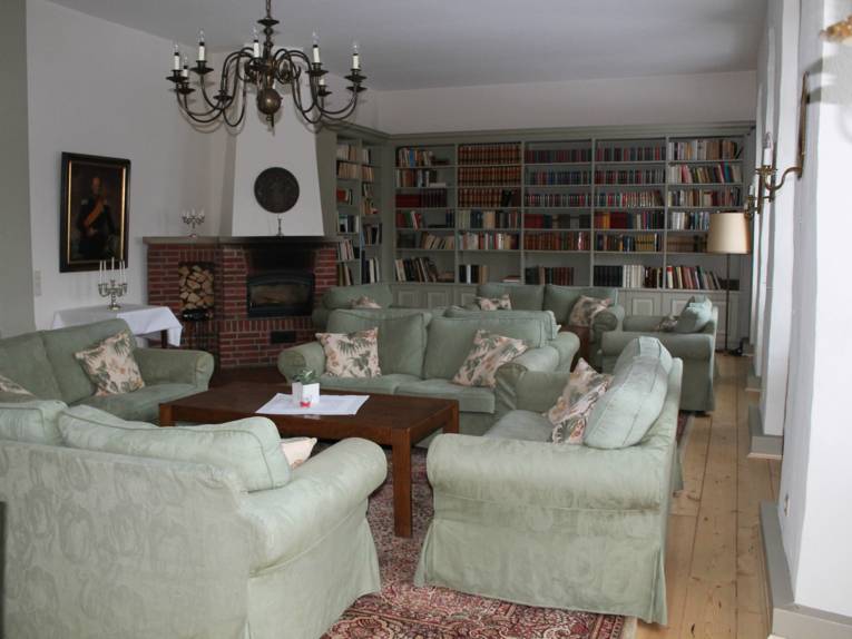 Das Kaminzimmer im Johanniterhaus. Aufgepolsterte Möbel, eine riesige Bücherregalwand und ein aus Stein gebauter Kamin.
