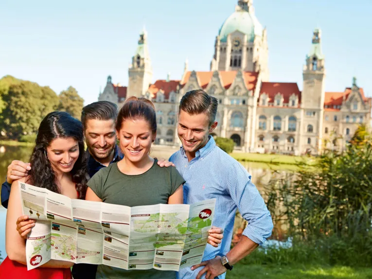 Four young adults look at a map of the city in front of the historic New Town Hall with its green dome.