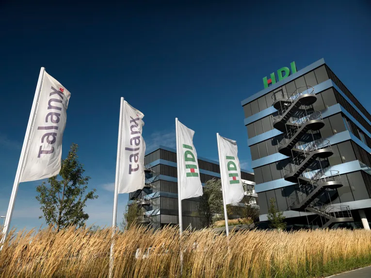 Flags with company logos are hoisted in front of a modern office building.