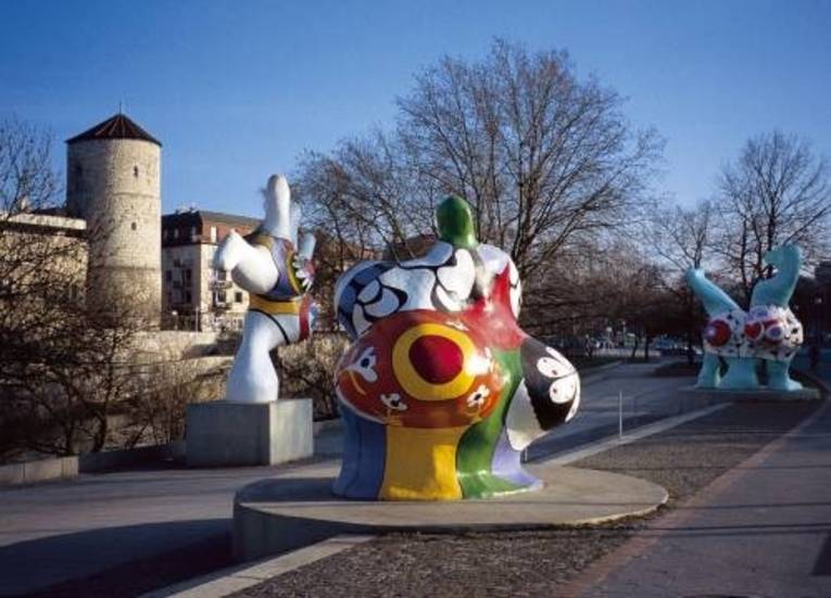 Skulpturen. Im Hintergrund eine Mauer und ein Turm. 