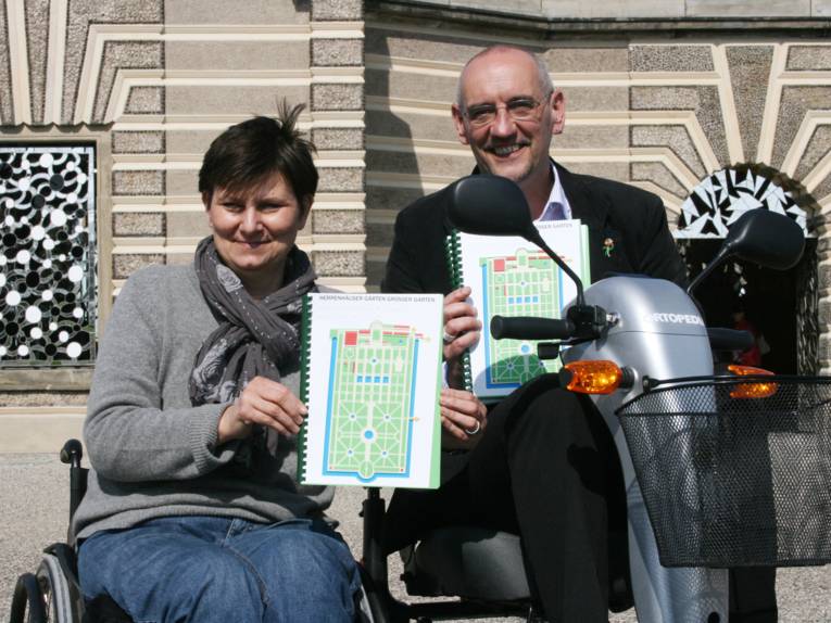 Andrea Hammann, Beauftragte für Menschen mit Behinderung der Landeshauptstadt Hannover, und Gartendirektor Ronald Clark präsentieren die Reliefpläne und die E-Scooter