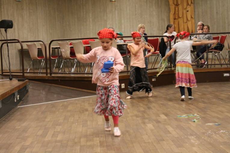 Drei Mädchen tanzen in Putzfrau-Kostümen durch den Saal und verstreuen Konfetti.