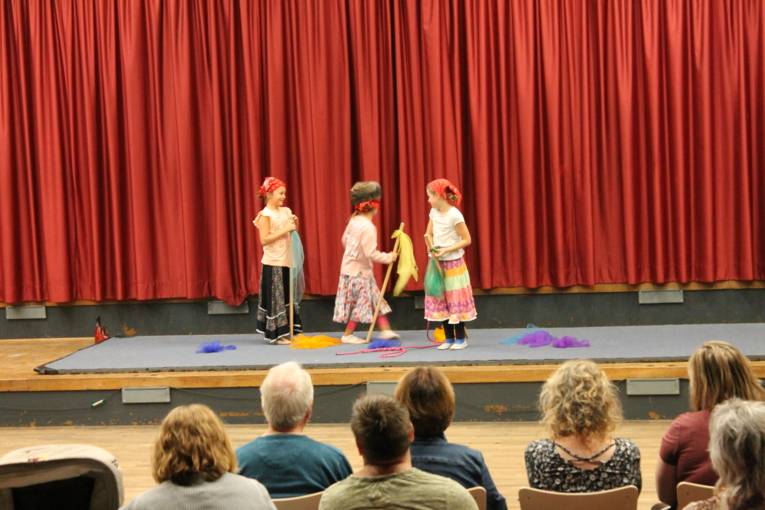 Auf einer Bühne stehen drei Mädchen in Putzfrauen-Kostümen und spielen eine Clownsnummer.