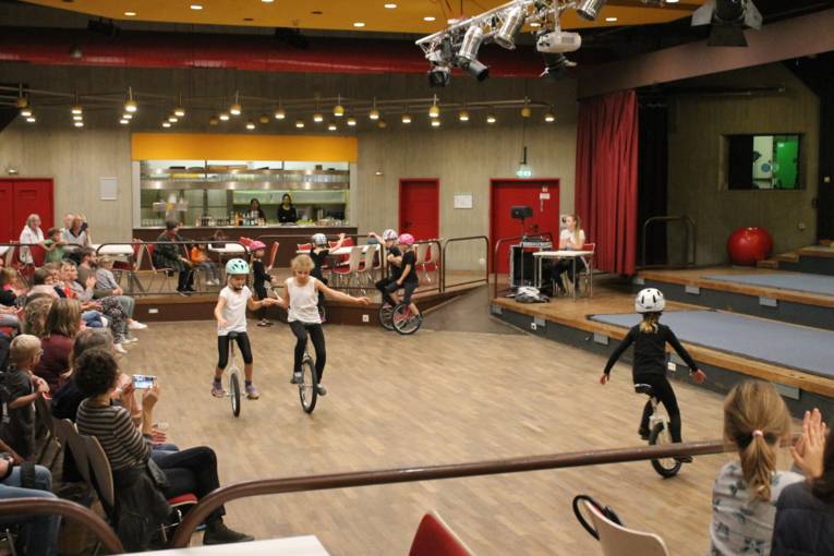 Mehrere Mädchen fahren in der Mitte des Saales mit ihren Einrädern. Links sitzt das Publikum und klatsch begeistert Beifall.
