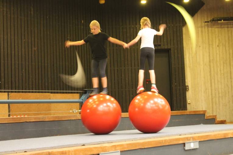Zwei Mädchen laufen hochkonzentriert auf je einer Kugel. Sie schwingen dabei bunte Tücher.