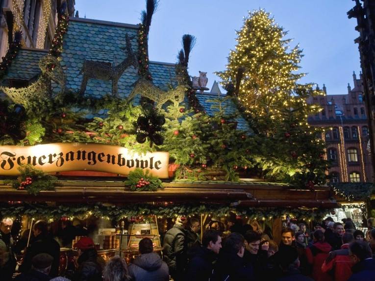 A stand decorated for Christmas with the illuminated sign "Feuerzangenbowle" on the market square next to the Marktkirche
