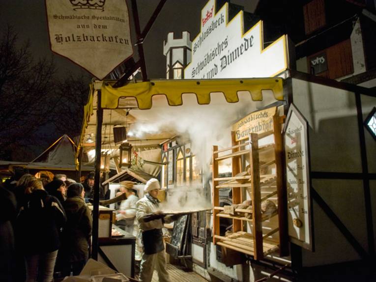 A man dressed as a baker pulls a steaming baking sheet out of a wood-fired oven in front of a large crowd.