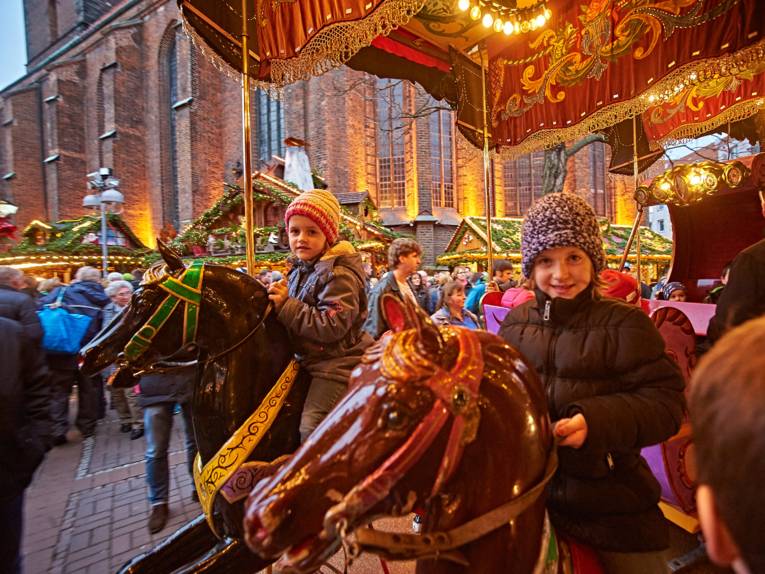 Two girls are sitting on wooden horses on a historic carousel at the Christmas market