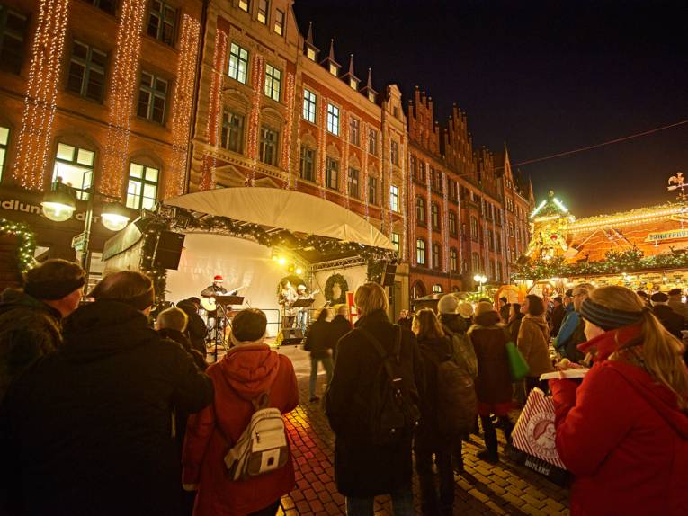 Three musicians on the stage set up in front of the bookstore at the Marktkirche are playing for the audience at the Christmas market