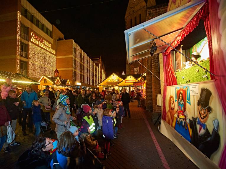 Parents and children watch the action on the puppet stage in the town square with great interest