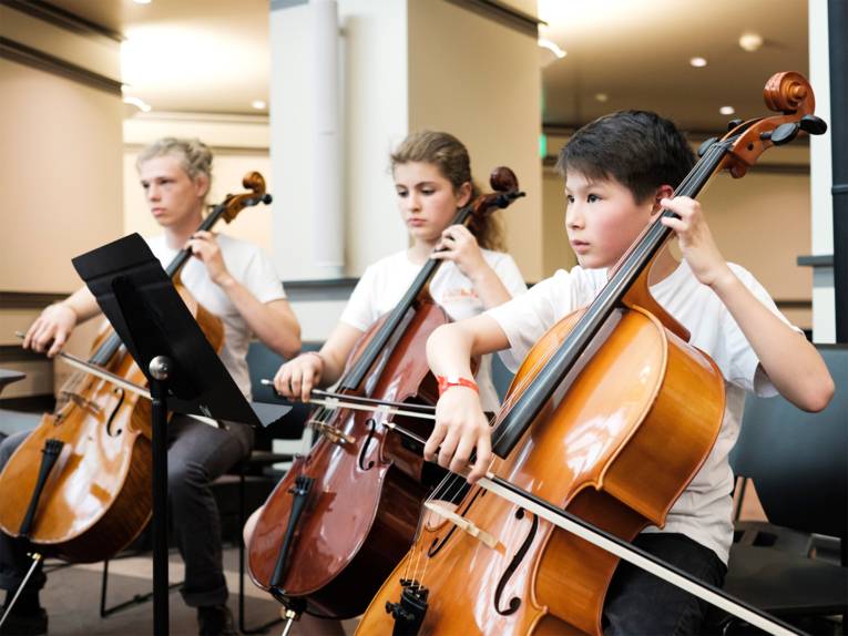 Zwei Schüler und eine Schülerin mit Streichinstrumenten (Cello/Kontrabass) spielen auf der Bühne