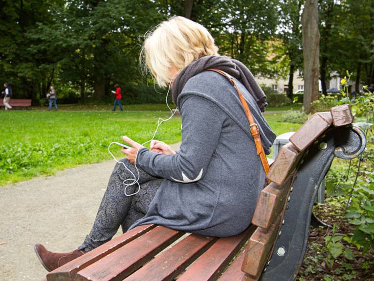 Eine Frau sitzt auf einer Parkbank und lauscht dem Audioguide