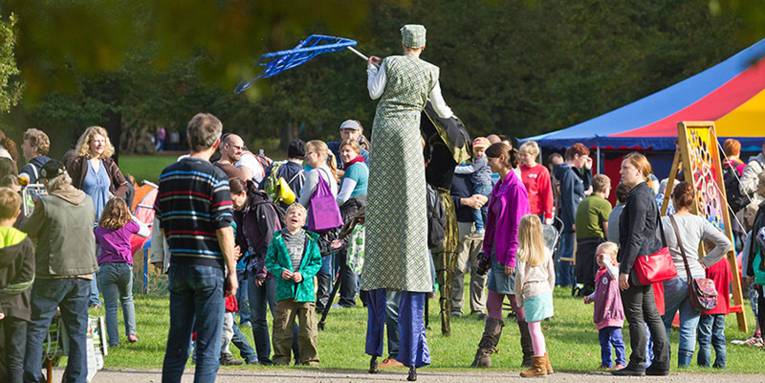A person dressed up as a forest ghost on stilts amidst visitors to the Tiergarten Festival.