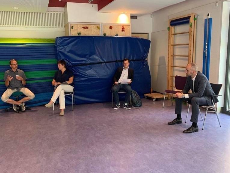 Vier Personen im Gespräch. Sie sitzen in einem Saal und halten Abstand. 