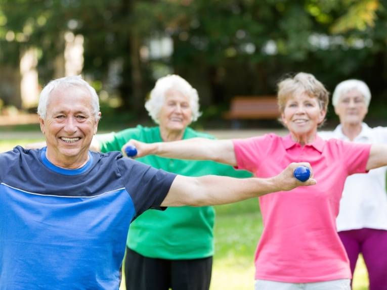 Drei ältere Frauen und ein älterer Herr in Sportkleidung bei der Gymnastik im Freien
