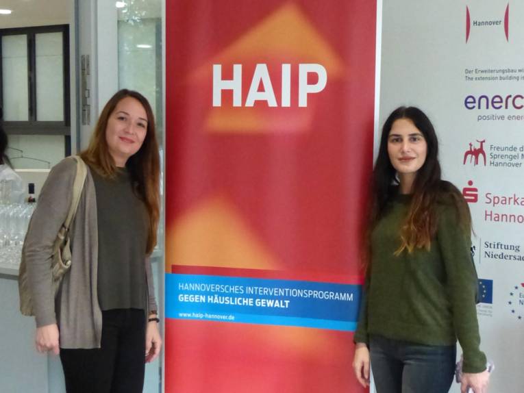 Zwei Frauen stehen neben einem großen Aufsteller mit der Aufschrift "HAIP-Hannoversches Interventionsprogramm gegen Häusliche Gewalt".