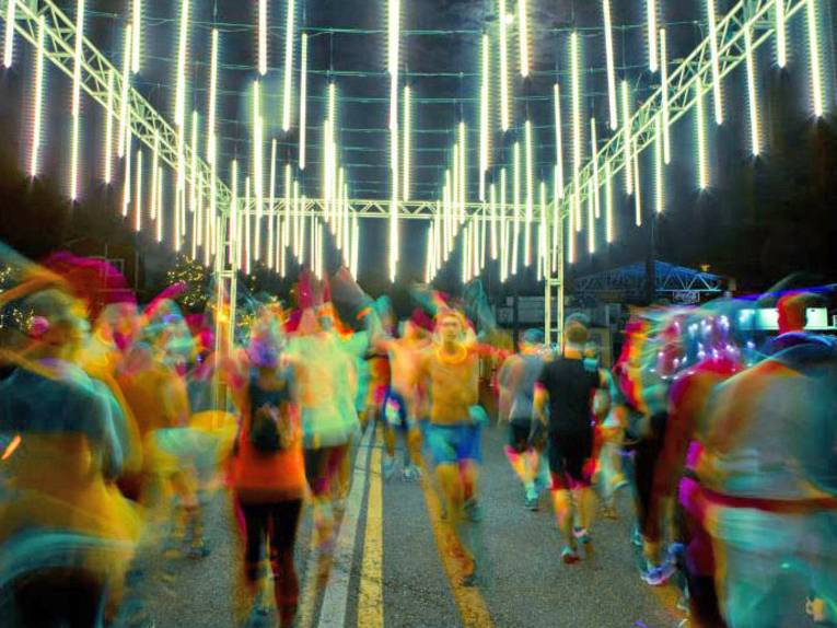 Mit bunten Leuchtmitteln behangene Läufer auf einem beleuchteten Parcours.