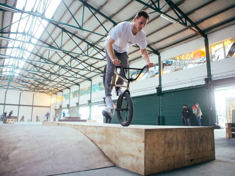 Ein BMX-Fahrer fährt auf dem Vorderrad über eine Rampe.