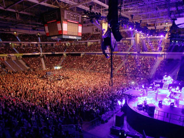 Buntes Schweinwerferlicht und Tausende Menschen: Eine Innenansicht der TUI Arena während eines Konzerts.