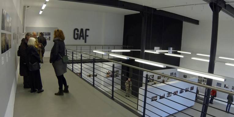 Ausstellungshalle, bei der auf zwei Ebenen Fotos an Wände und Stellwände angebracht sind. 