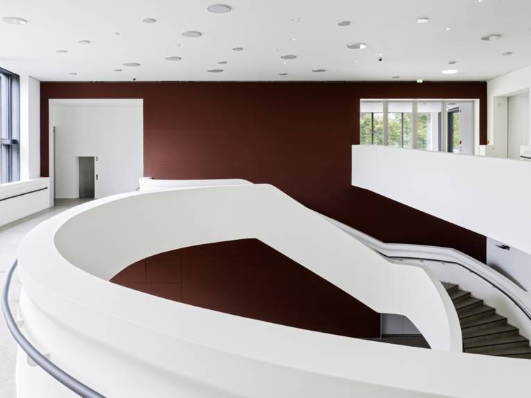 Blick in einen großen zweigeschossigem Raum, in dem ein lang geschwungener runder Aufgang die beiden Etagen miteinander verbindet.