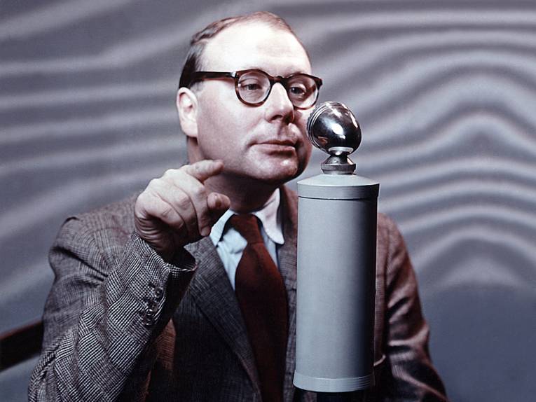 Foto eines Mannes mit Brille vor einem Radiomikrofon.