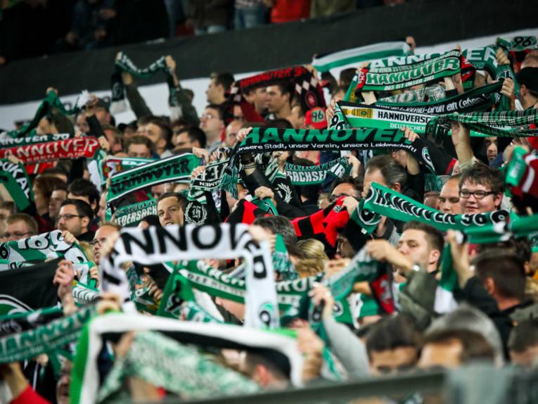 Fußballfans im Stadion halten Schals mit der Aufschrift "Hannover 96" in die Höhe.