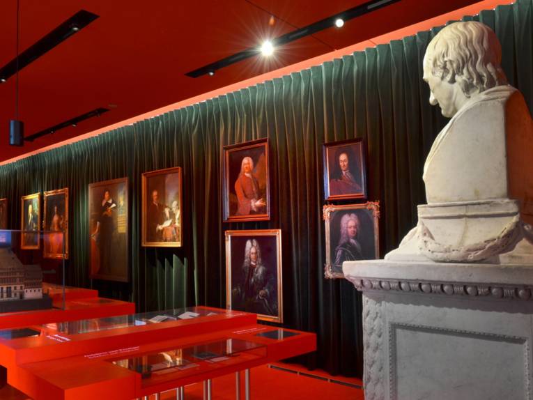 Utsikt inn i barokkfløyen på museet Schloss Herrenhausen; i forgrunnen til høyre står en byste av universalgeleften Leibniz, og i bakgrunnen henger ulike portrettmalerier foran et grønt fløyelsgardin