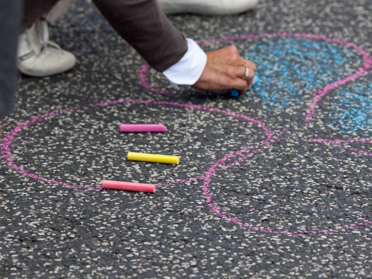 Eine Hand malt mit bunter Kreide auf grauem Asphalt