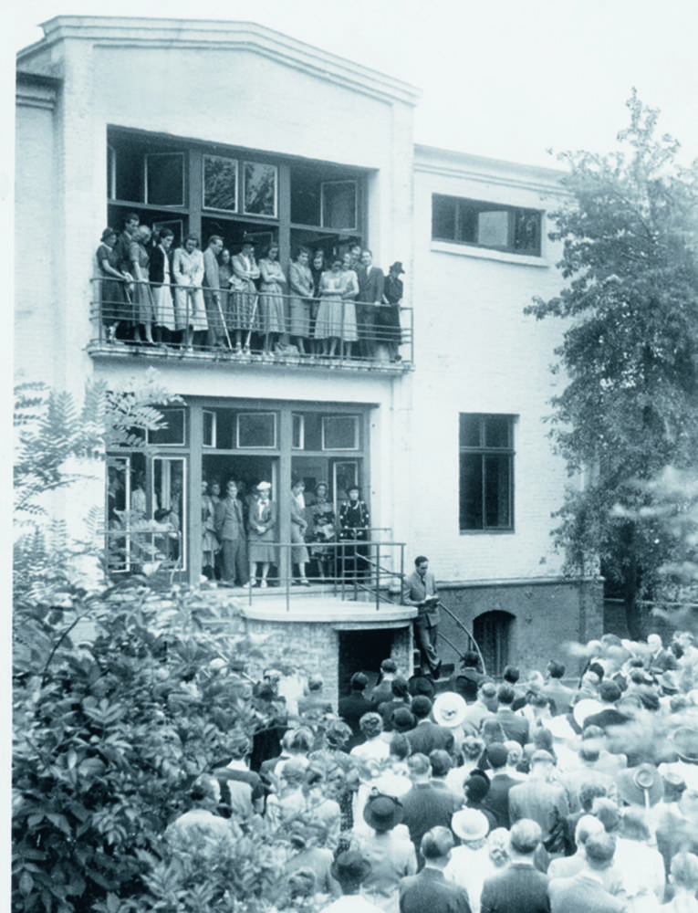 Viele Menschen vor einem Gebäude sowie auf Balkonen des Gebäudes