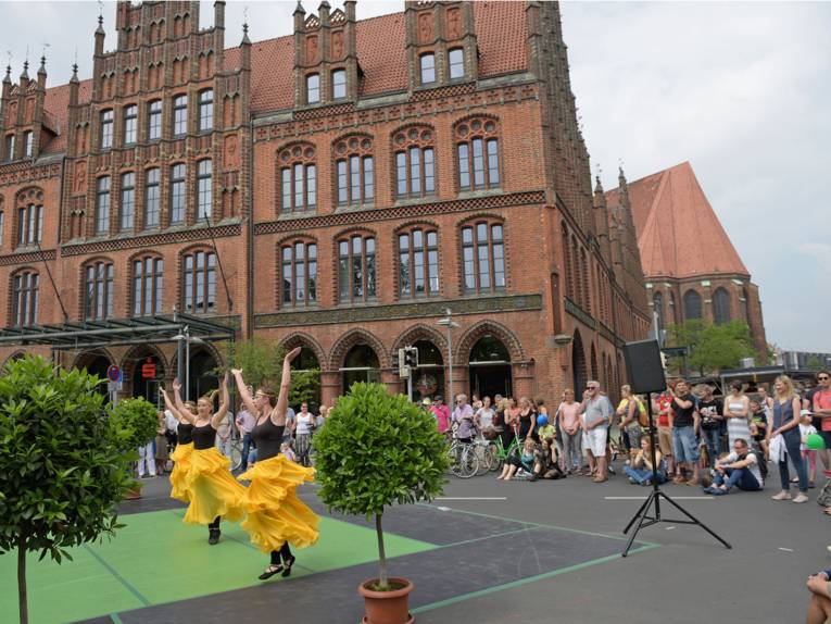 Drei Tänzerinnen auf der Straßenbühne vor dem Alten Rathaus in Hannover sind von Zuschauerinnen und Zuschauern umringt.