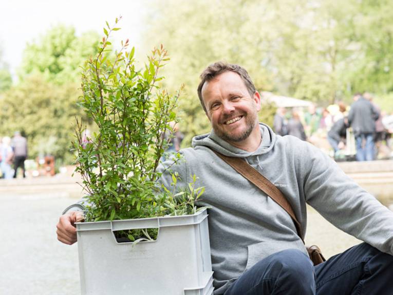 Ein fröhlicher Mann hält eine Plastikbox mit Pflanzeneinkäufen