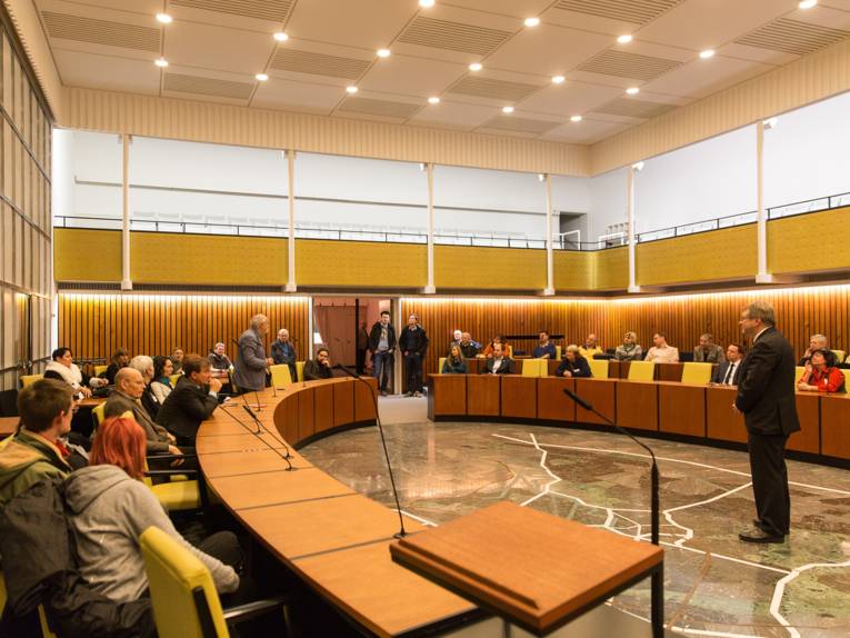 Bürgermeister Hermann spricht im Ratssaal zu Besucherinnen und Besuchern und erklärt ihnen den Ablauf einer Ratsversammlung